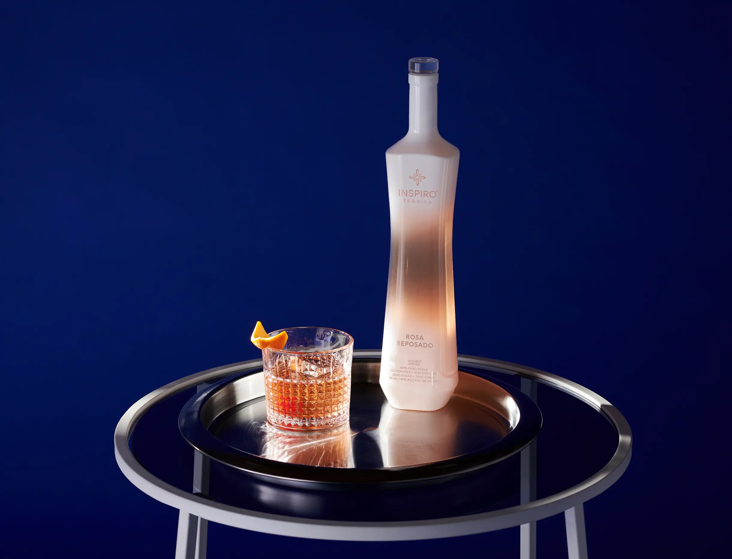 Bottle of Inspiro Tequila Rosa Reposado on a dark surface with a blue background