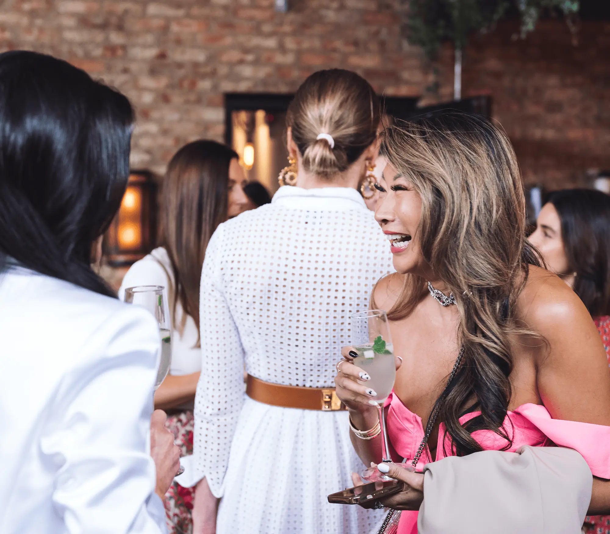 Woman holding an Inspiro Tequila cocktail at a social event with brick wall background