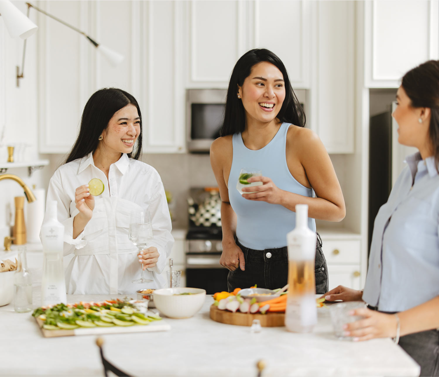 Three women socializing in a kitchen with a snack platter and Inspiro Tequila.