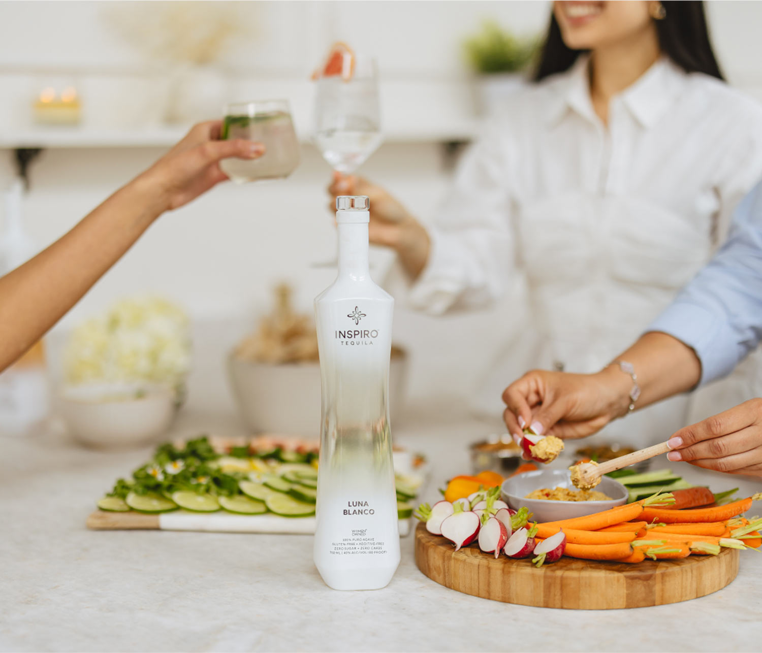 Bottle of Inspiro Luna Blanco tequila on a table with people enjoying a snack platter.
