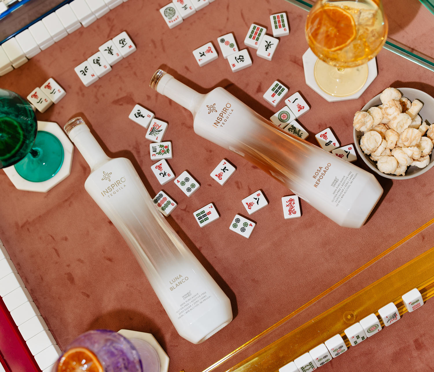 Two bottles of Inspiro Tequila on a table with mahjong tiles and snacks.
