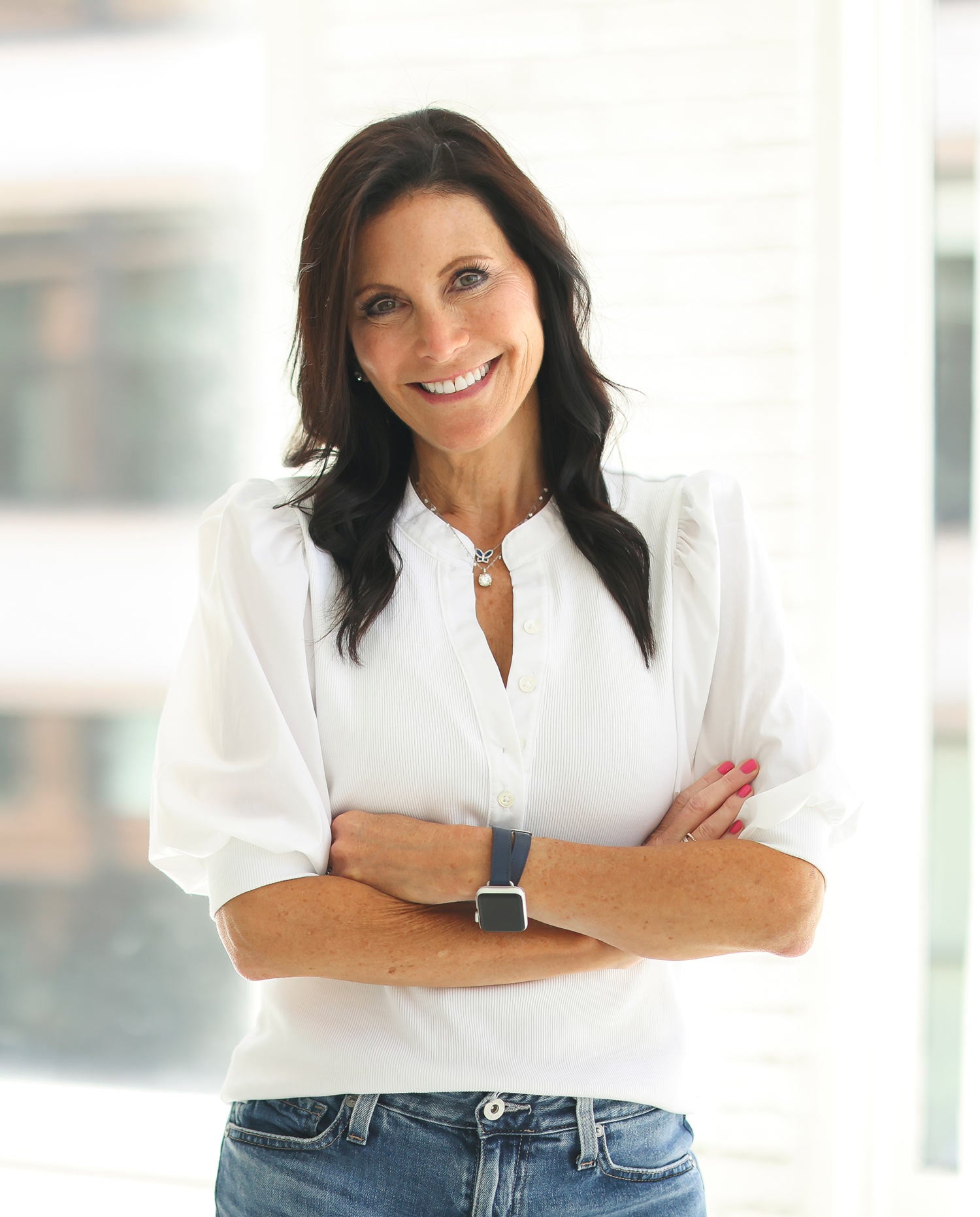 Founder Mara Smith in white blouse and jeans standing with arms crossed in a bright room.