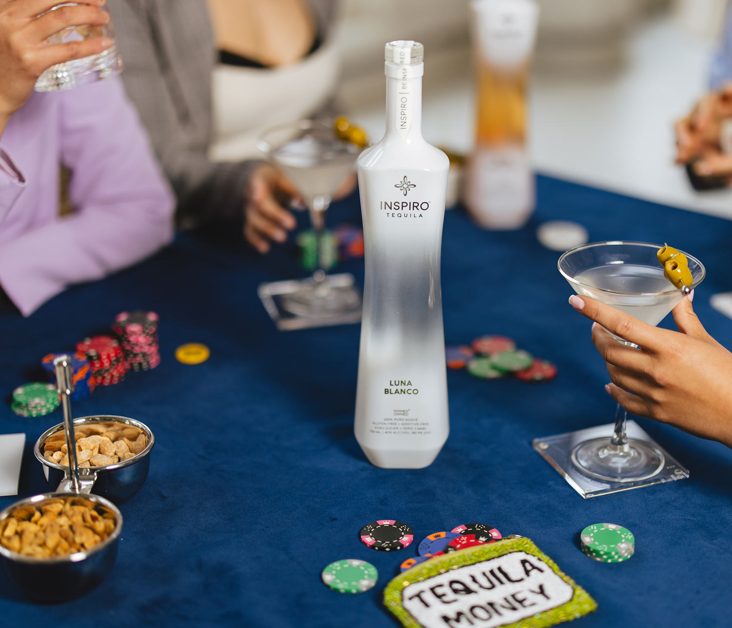 Inspiro Tequila bottle and cocktail on a table with people socializing.