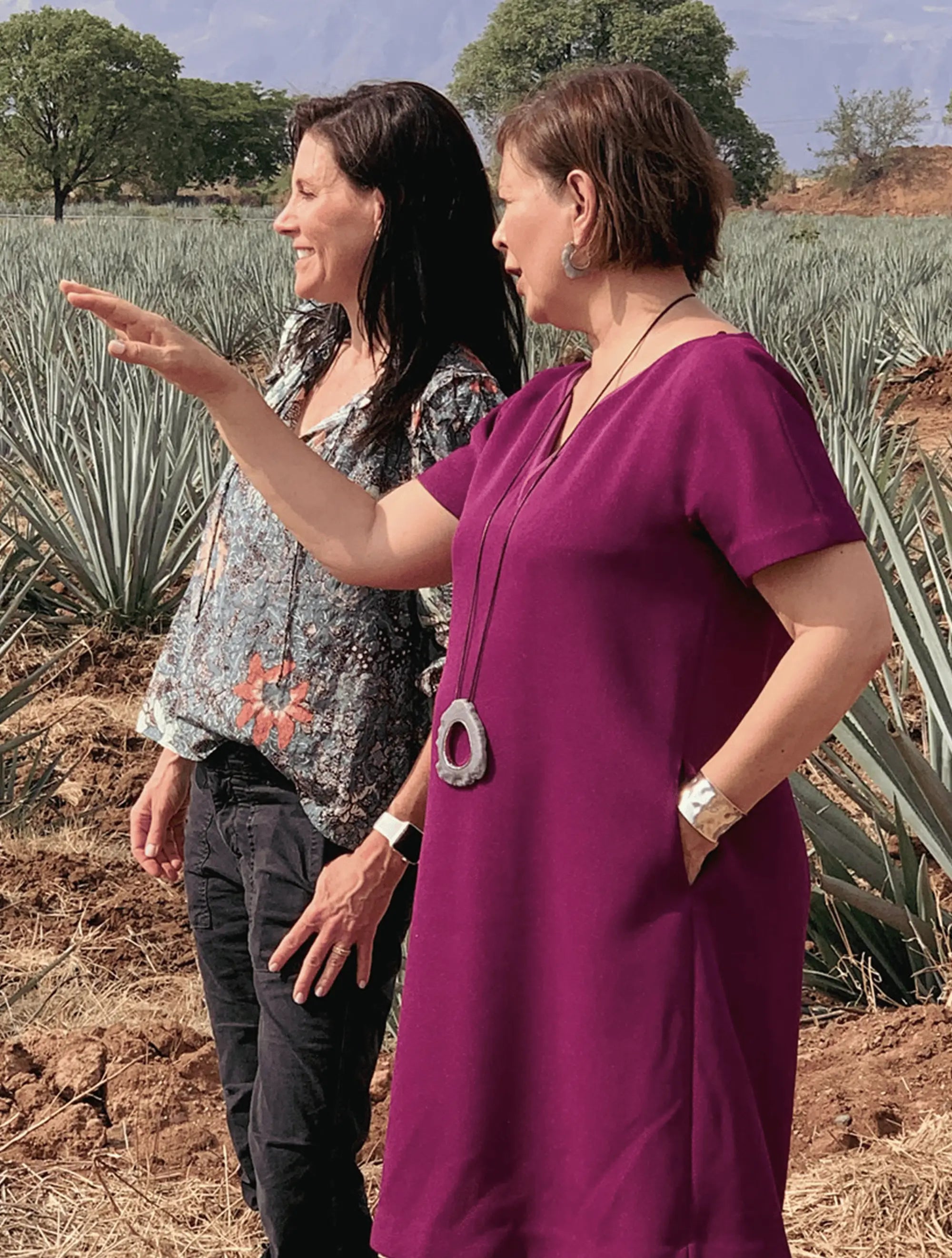 Mara Smith and another Person standing in a field with agave plants, one pointing towards the plants.