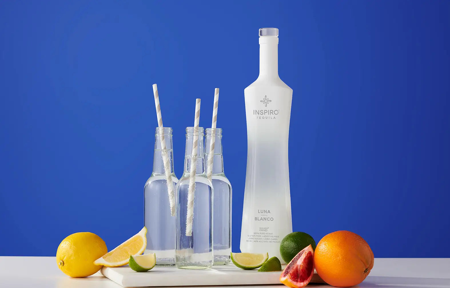 Bottle of Inspiro Tequila with glasses and fruits on a blue background