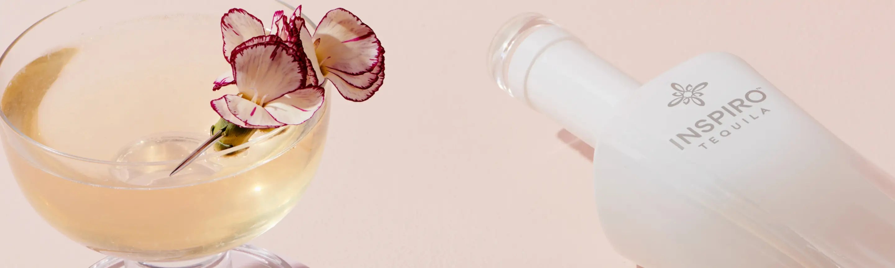 Bottle of Inspiro Tequila with a glass of drink and flowers on a light pink background