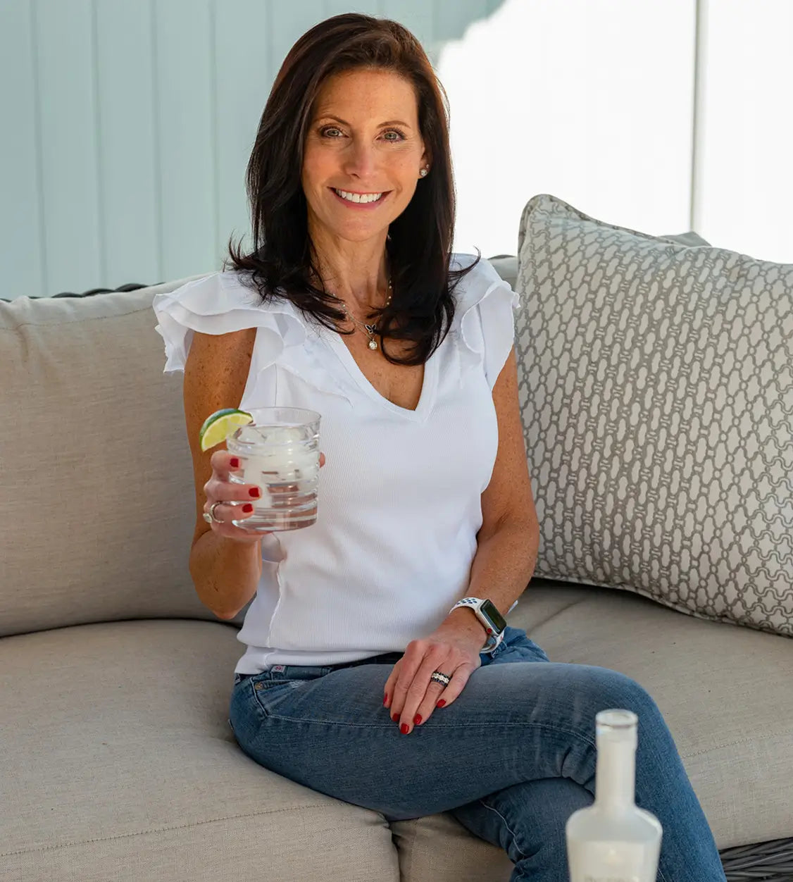 Mara Smith sitting on a couch holding a glass of Inspiro Tequila cocktail and smiling.