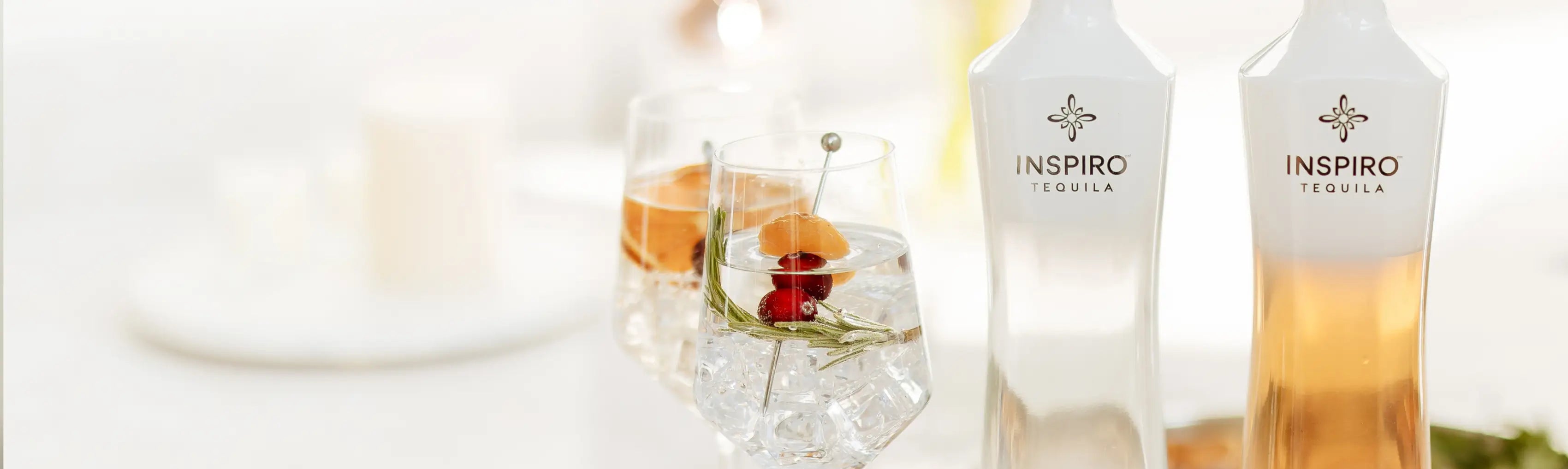 Two bottles of Inspiro Tequila on a white background with two glasses of cocktails