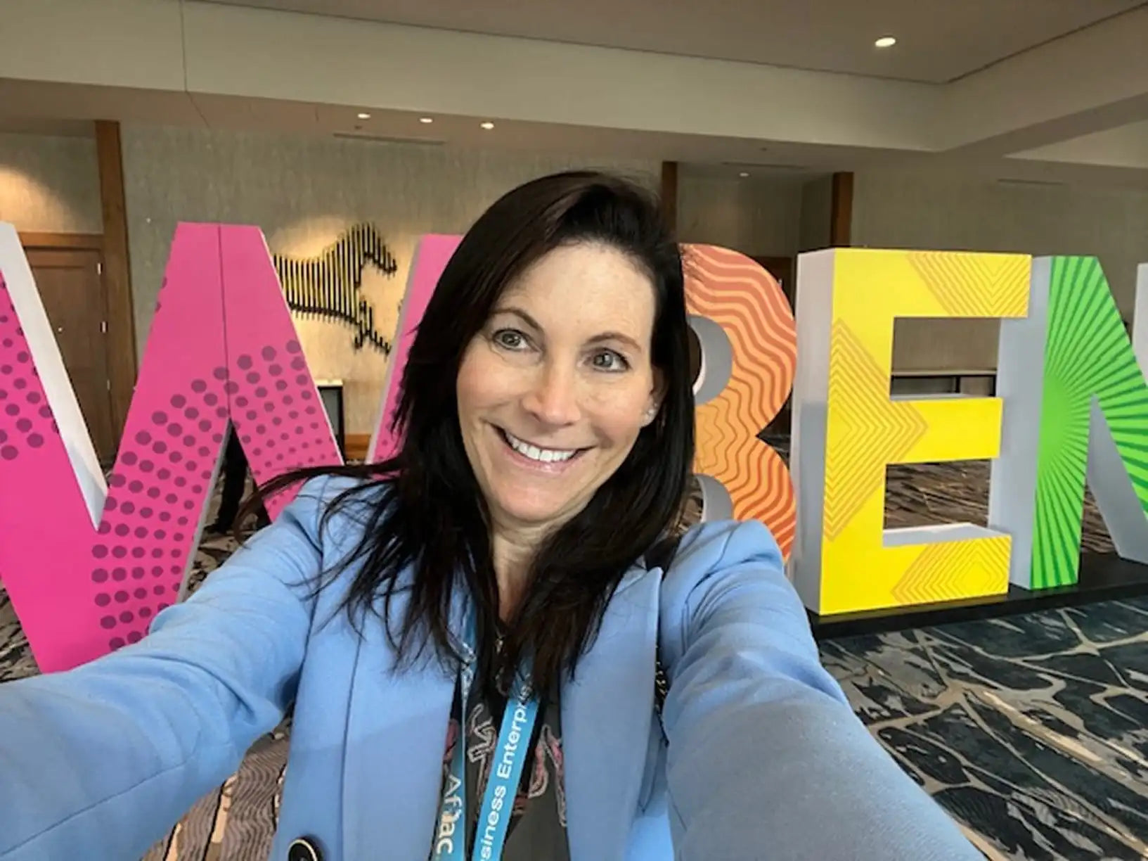 Mara Smith taking a selfie in front of colorful letters spelling 'WELCOME' in a modern interior setting.