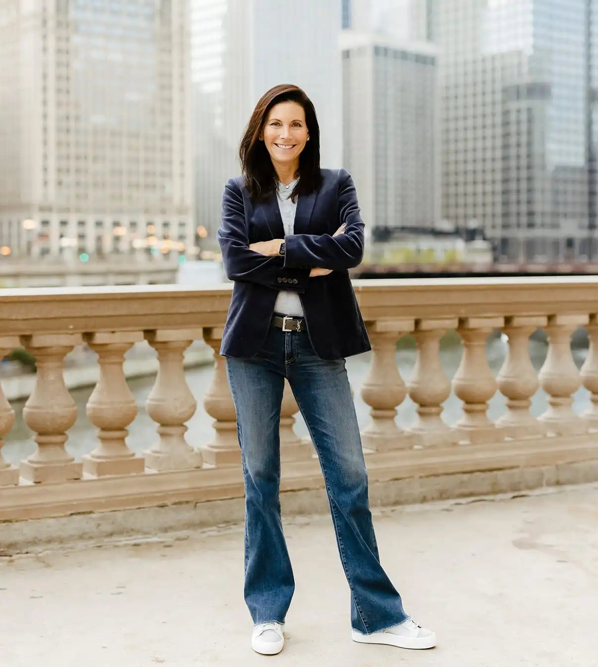 Mara Smith in a suit and jeans standing in front of a cityscape